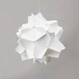 A white matte pendant lamp shade with a geometric design, featuring precisely cut rectangles and softly rounded corners, suspended from a ceiling.