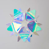 Small pink and blue iridescent spherical lampshade with star- or petal-like patterns, hanging from the ceiling with the light turned off.