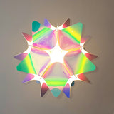 Top view of a pink and blue iridescent spherical lampshade with star- or petal-like patterns, hanging from the ceiling with the light turned off.